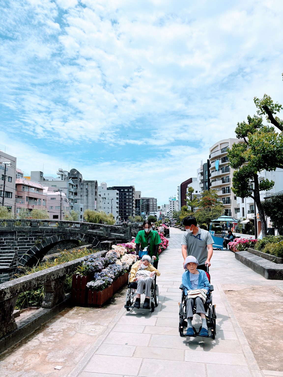 介護施設の入居者とスタッフが川沿いの遊歩道を散歩している風景